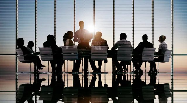 Silhouettes of business people in a meeting room with city view and sunlight.
