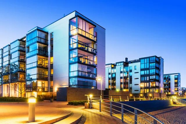 Modern apartment buildings illuminated at dusk by a waterfront.