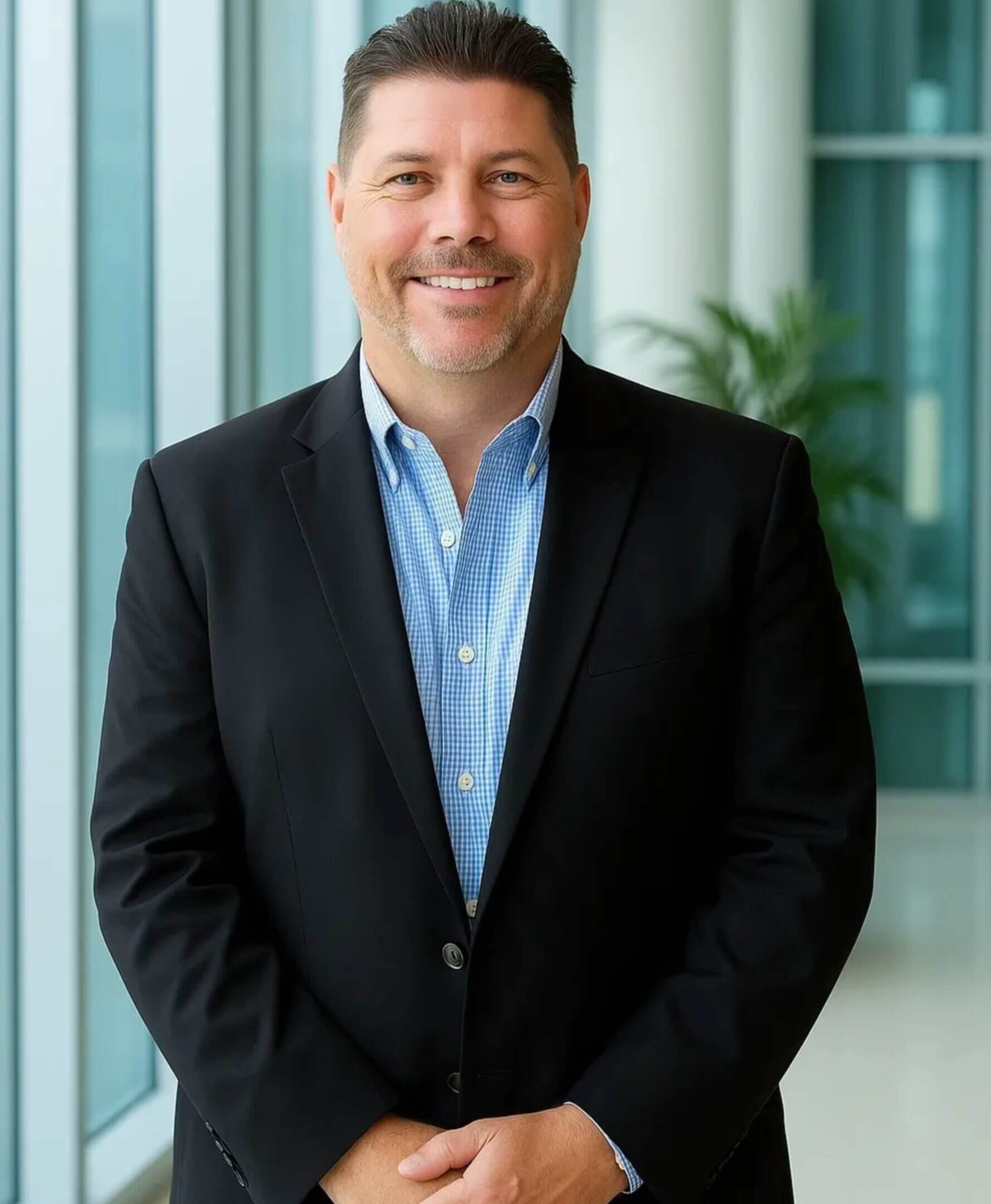 Man in suit smiling near large windows.
