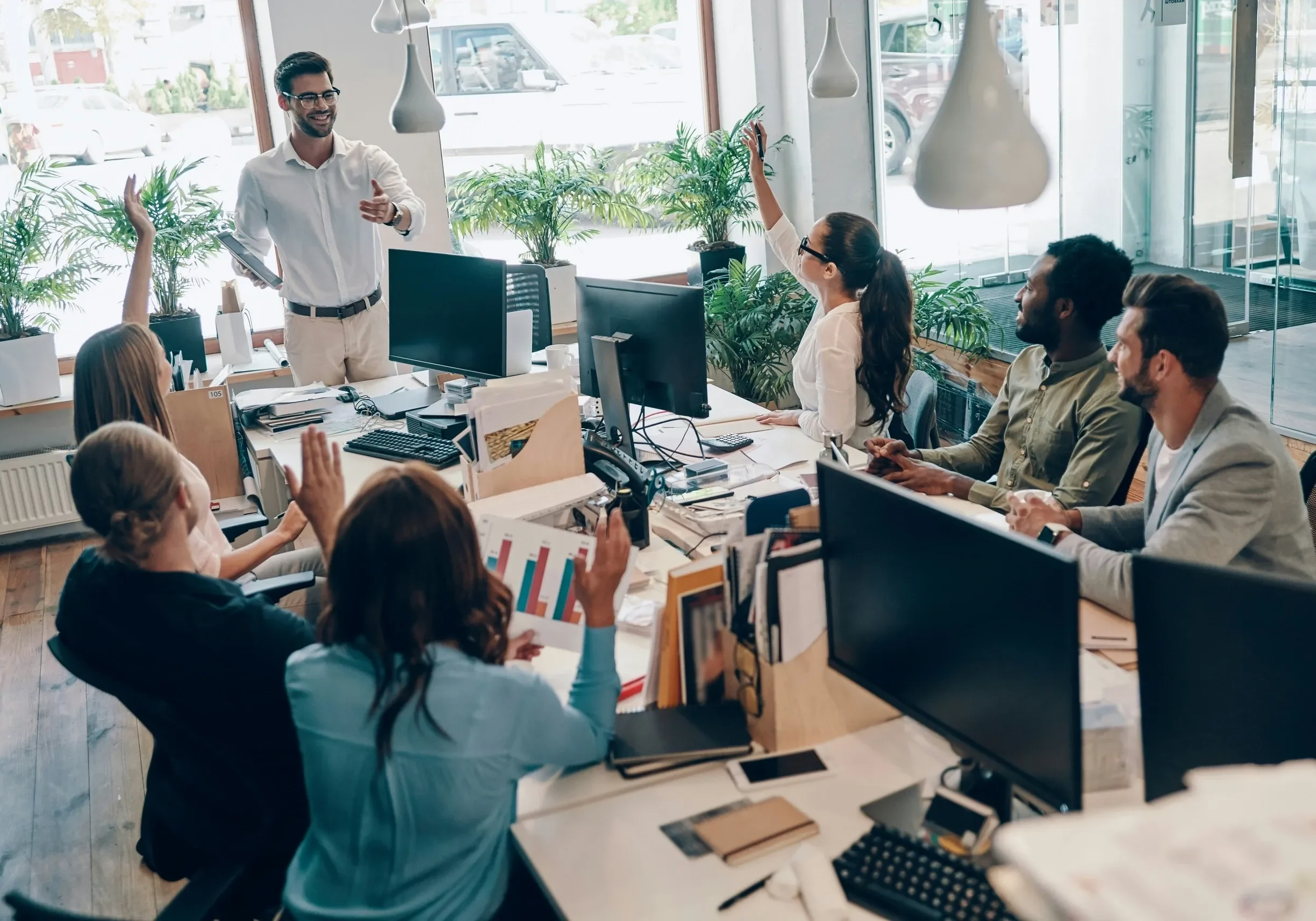 Coworkers raising hands during lively office meeting